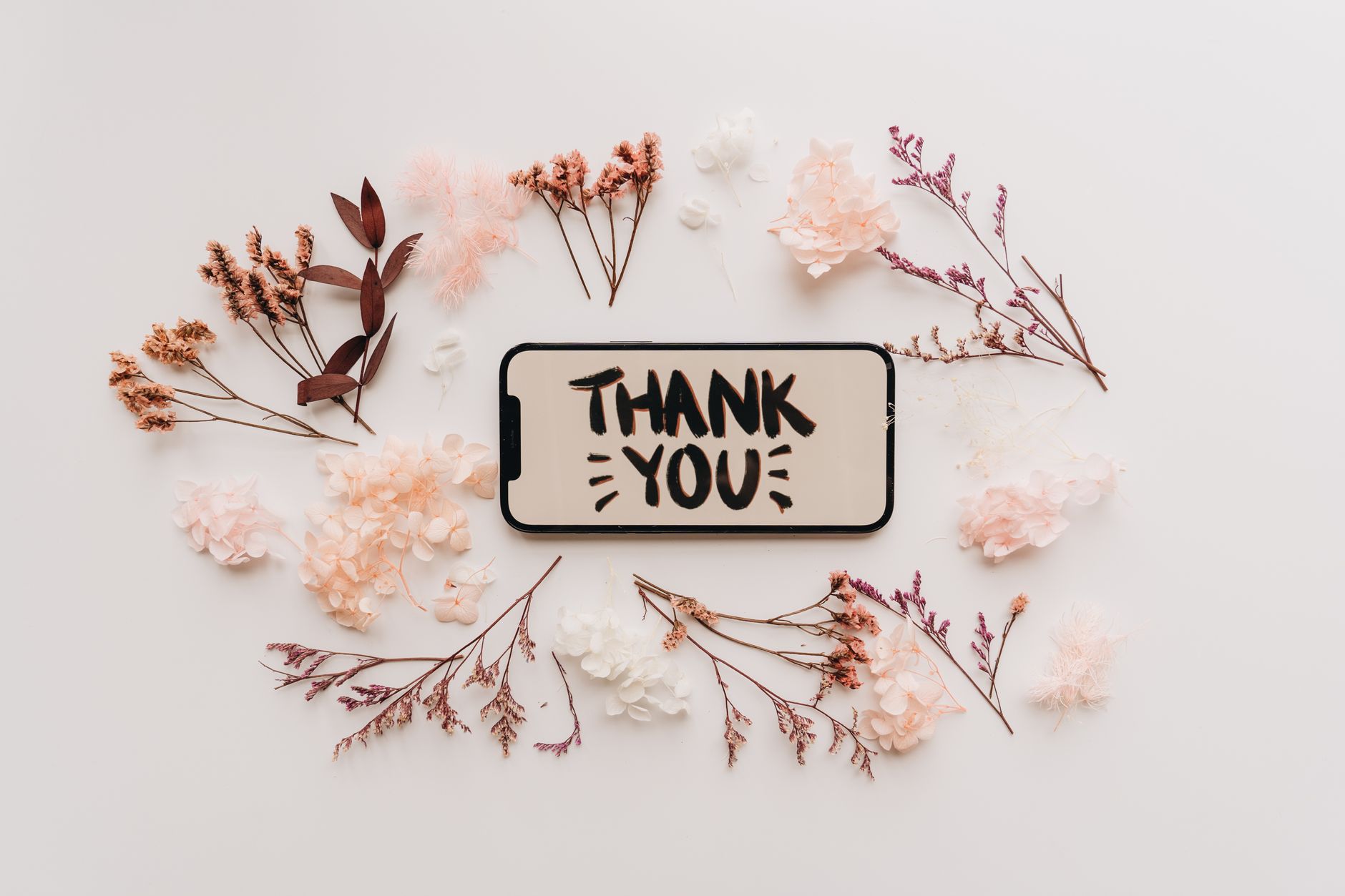 christian thank you messages for support - Flat lay of dried flowers surrounding a smartphone displaying a thank you message.