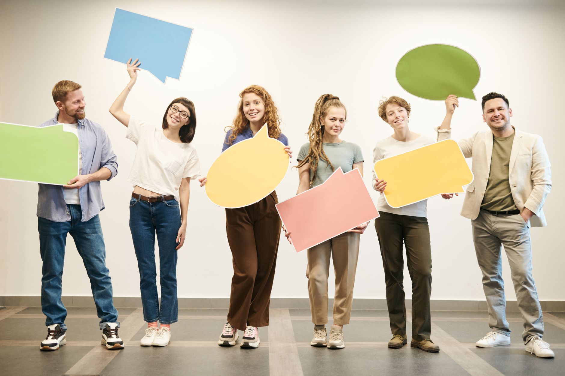 How to Adapt Messages for Different Customer Personalities - Diverse group of smiling adults holding vibrant speech bubbles indoors.