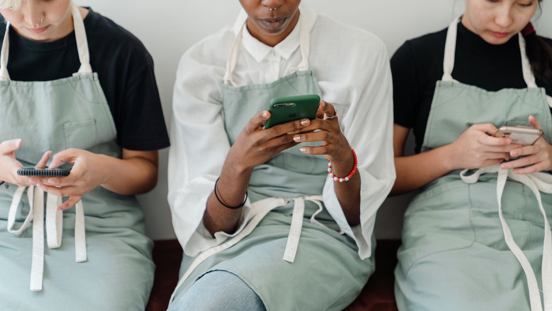 How to Adapt Messages for Different Customer Personalities - Unrecognizable diverse young females in casual clothes and aprons sitting together and messaging on mobile phones while resting on bench during break in cafe