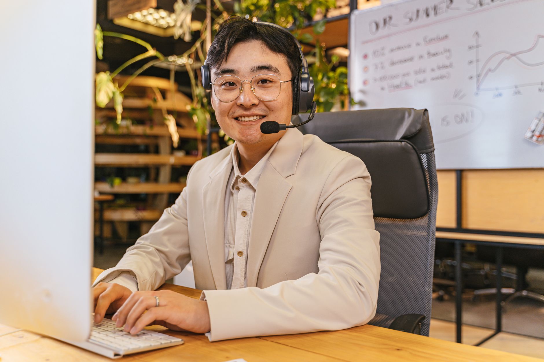 Message Support Strategies for Remote Teams - Smiling man with headphones in a stylish office environment, working on a computer.