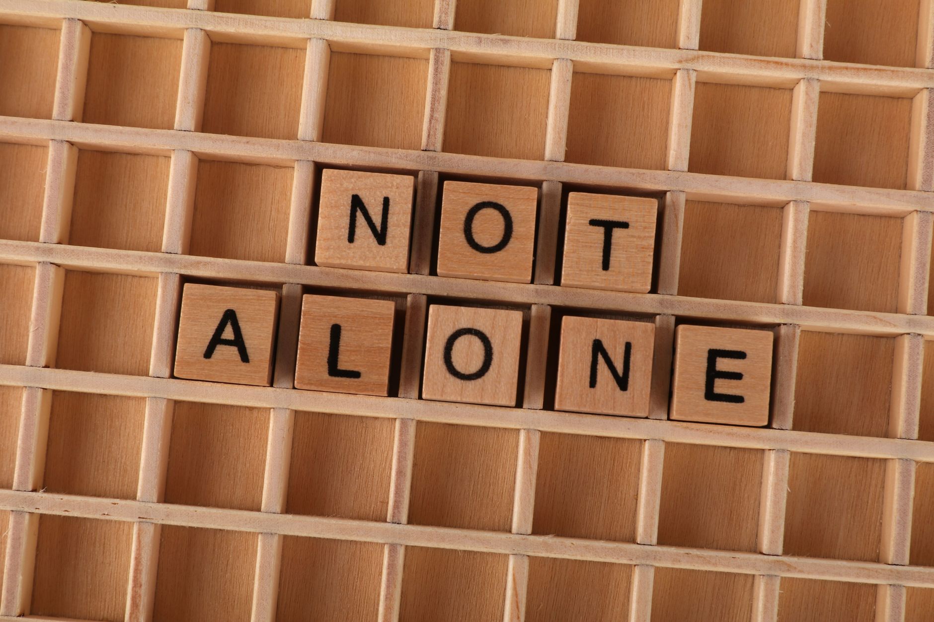 nonprofit organizations text messaging supporters engagement strategies - Wooden Scrabble tiles spelling 'Not Alone' on a wooden grid background, conveying support and connection.