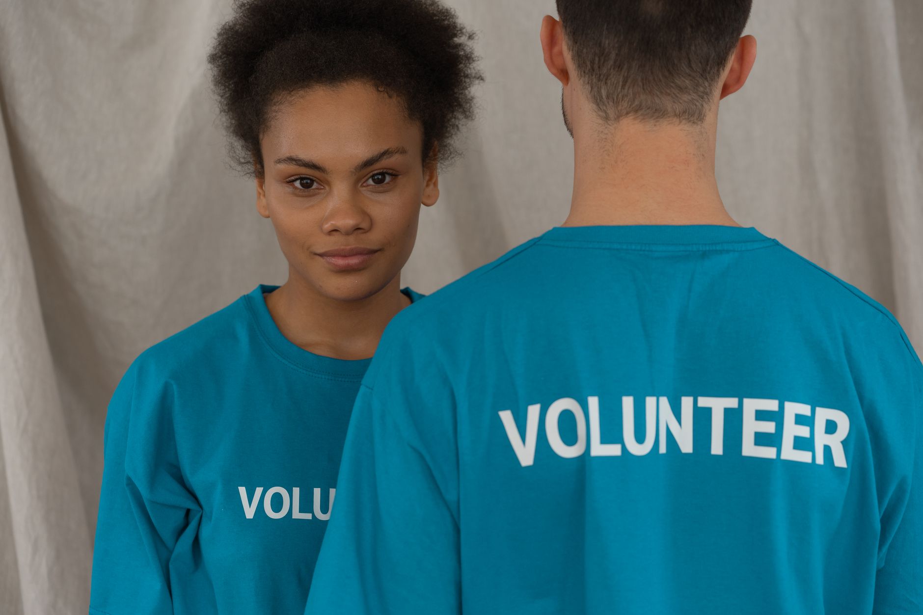 nonprofit organizations text messaging supporters fundraising - Two volunteers in blue shirts, one smiling and facing camera, promoting support and teamwork.