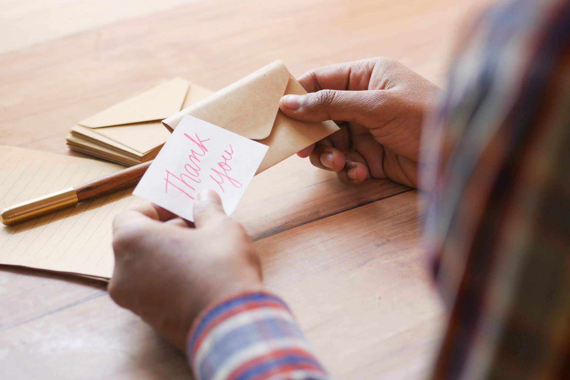 short thank you message for money support - Close-up of hands holding a thank you note in an envelope on a table.