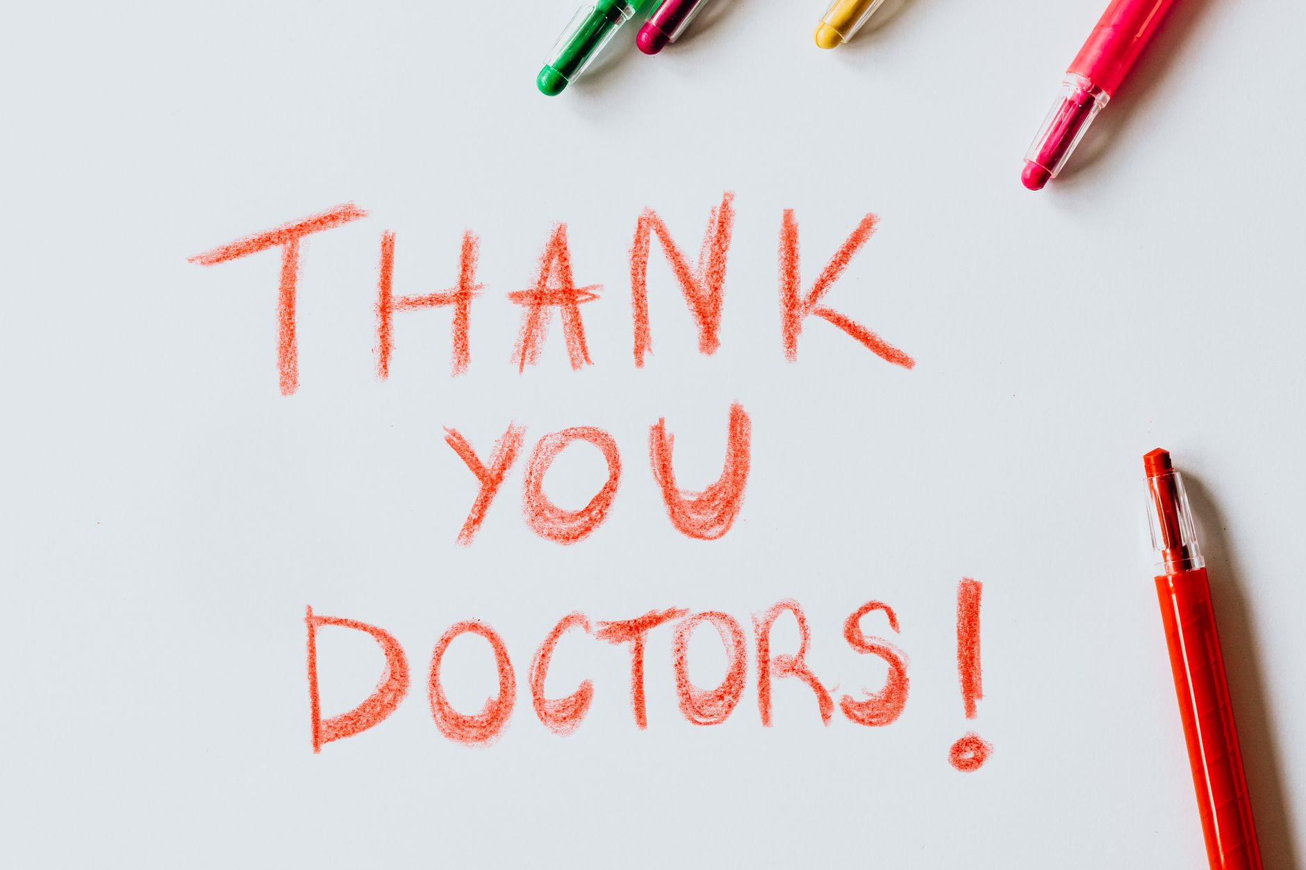 thank you message to church members for support - A handwritten 'Thank You Doctors!' note surrounded by colorful pens on a white surface.