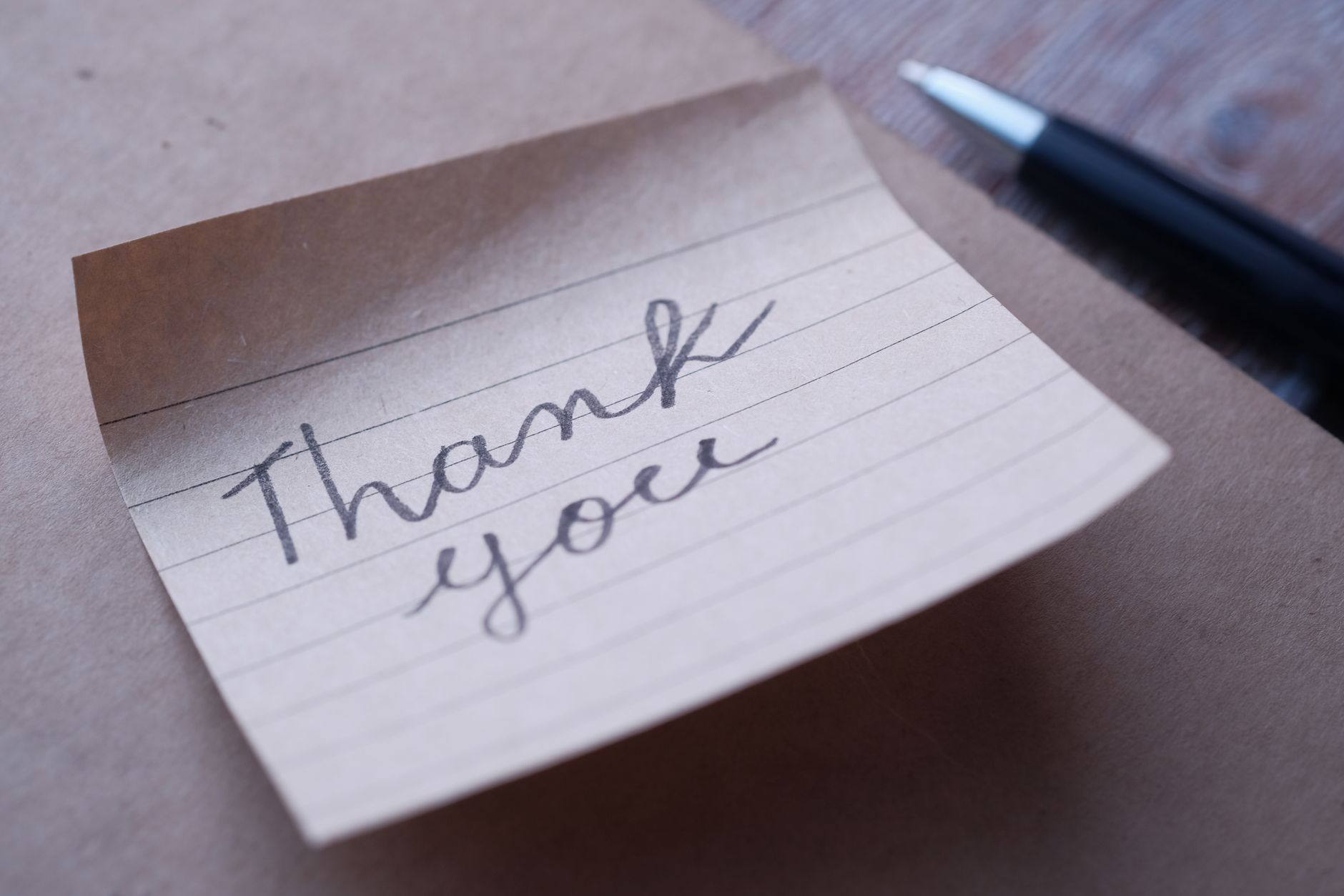 thank you messages for support - Close-up of a handwritten thank you note on brown paper with a pen nearby.