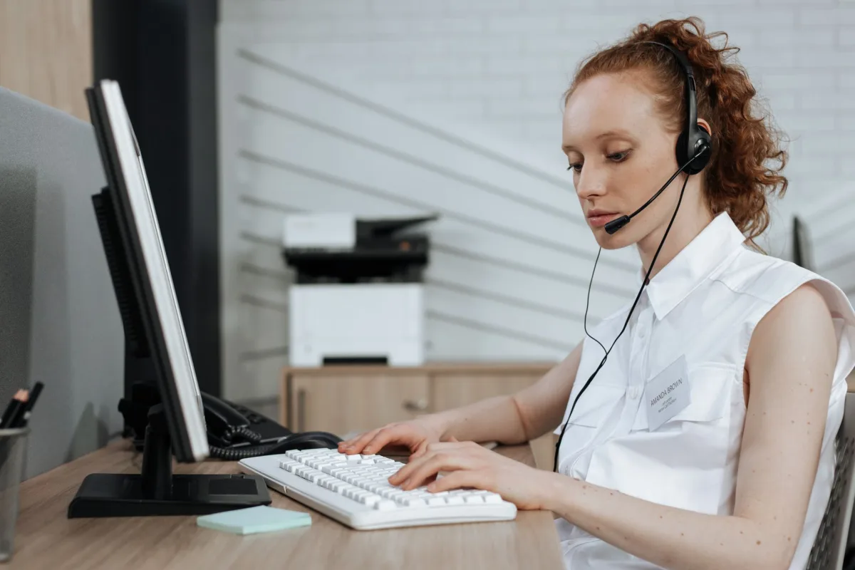 A female call center agent typing on a keyboard while wearing a headset at her desk. A female call center agent typing on a keyboard while wearing a headset at her desk.
