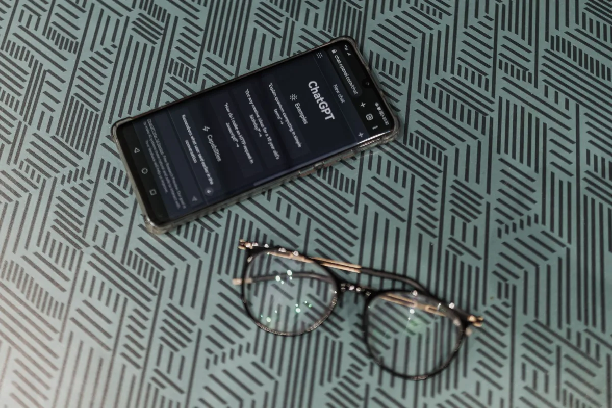 Close-up of smartphone displaying ChatGPT alongside eyeglasses on a patterned surface highlighting technology and style. Close-up of smartphone displaying ChatGPT alongside eyeglasses on a patterned surface highlighting technology and style.