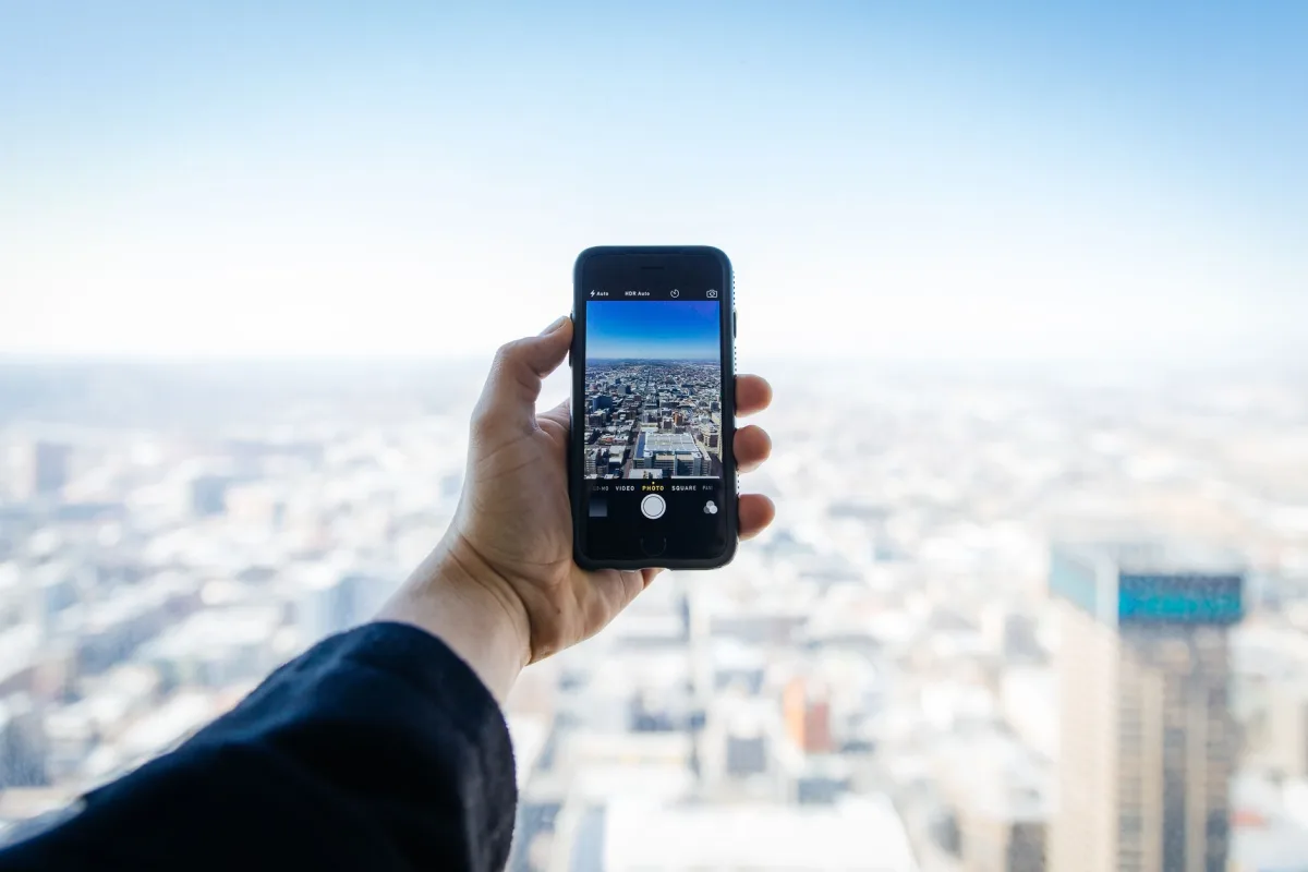 A hand holding a smartphone capturing an urban cityscape from above. A hand holding a smartphone capturing an urban cityscape from above.