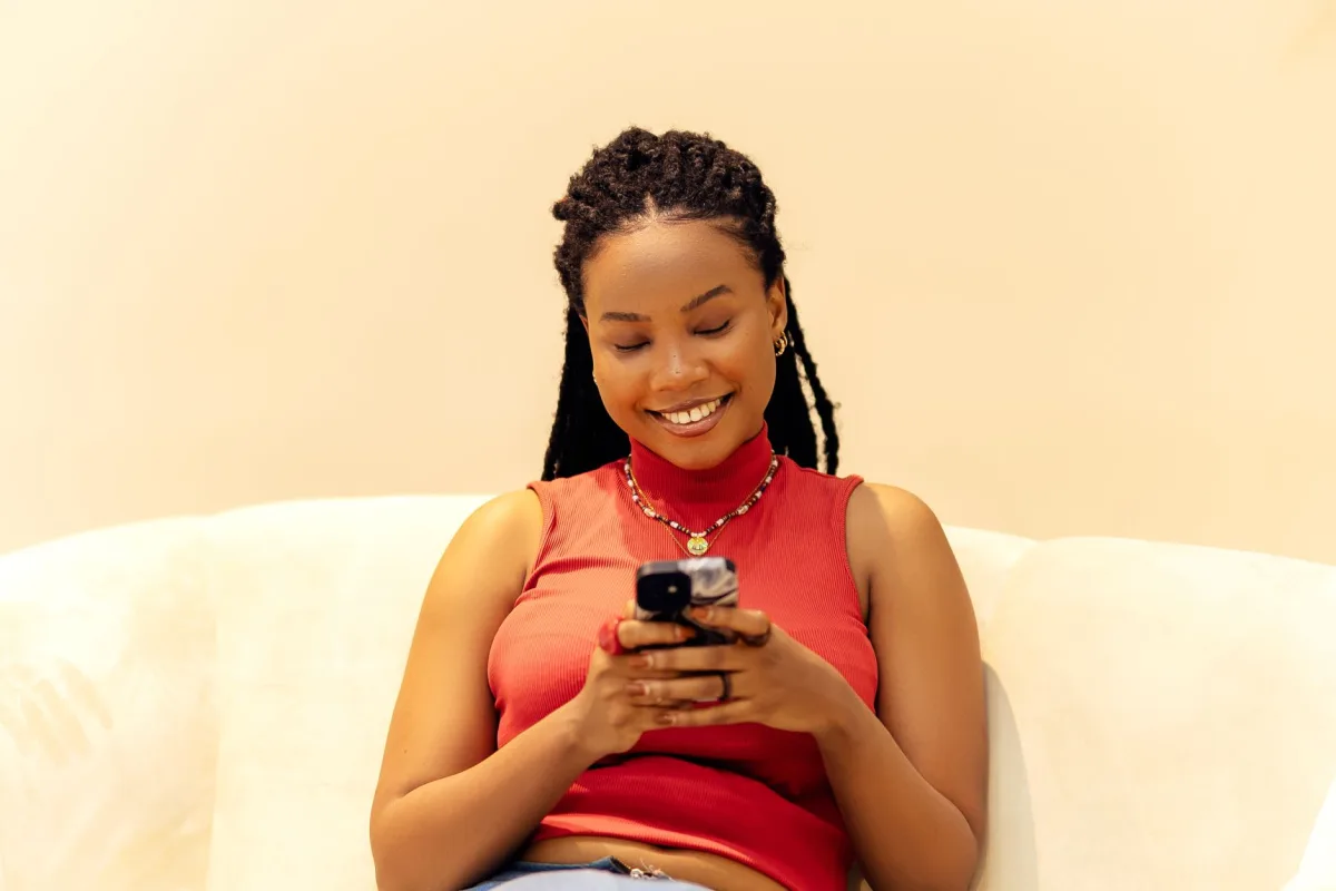 Woman with braided hair smiling while using a smartphone indoors. Woman with braided hair smiling while using a smartphone indoors.