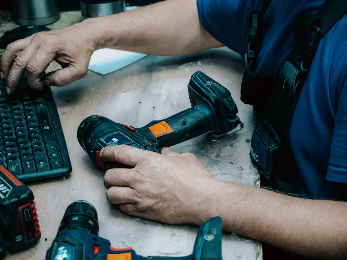 A technician operates a keyboard while holding a cordless drill at a workstation.