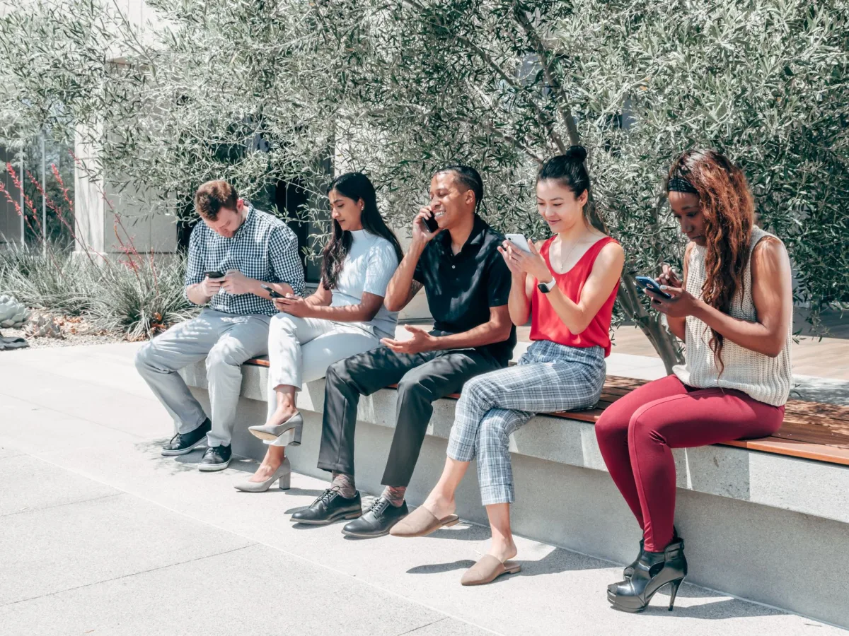 A diverse group of adults sitting outdoors using smartphones, communicating and browsing. A diverse group of adults sitting outdoors using smartphones, communicating and browsing.