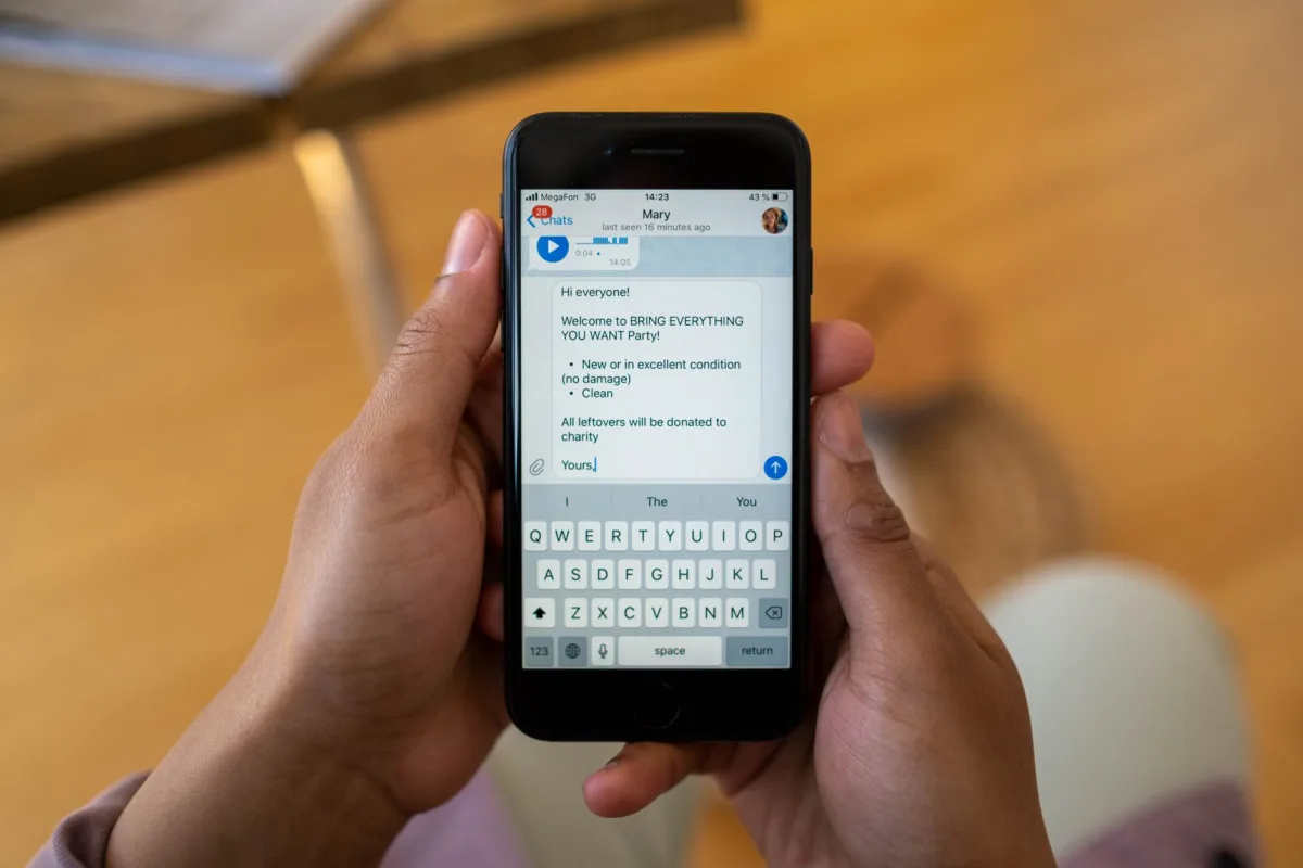 Person holding a smartphone displaying a text message about a party event indoors.