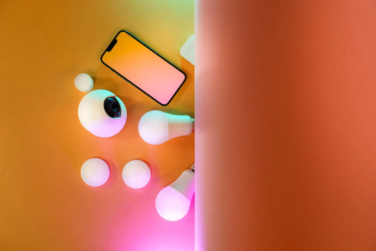 Top view of home gadgets including smartphone, camera, light bulbs in a colorful setup.