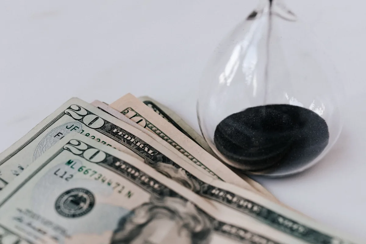From above transparent hourglass with flares on fragile surface near pile of banknotes with numbers official seal