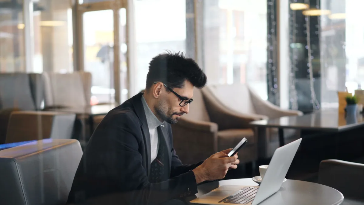 Man in formalwear smartphone and laptop in a modern café setting. Man in formalwear smartphone and laptop in a modern café setting.