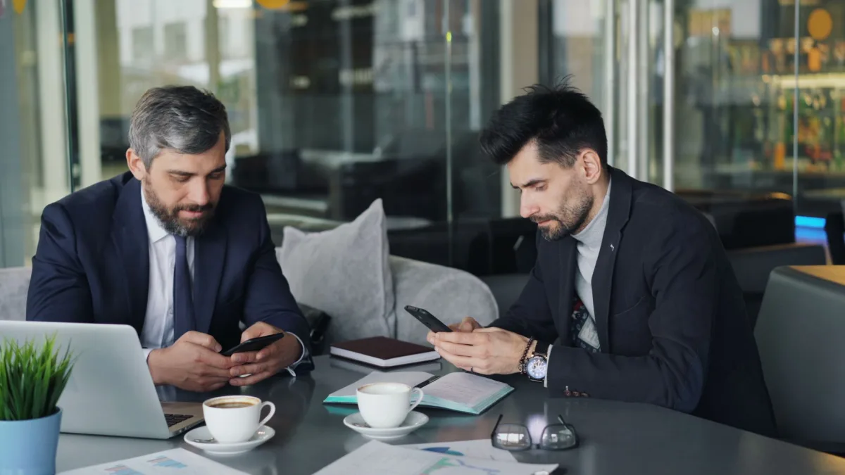 Two businessmen in a cafe working on smartphones and laptops, engaged in a meeting. Two businessmen in a cafe working on smartphones and laptops, engaged in a meeting.