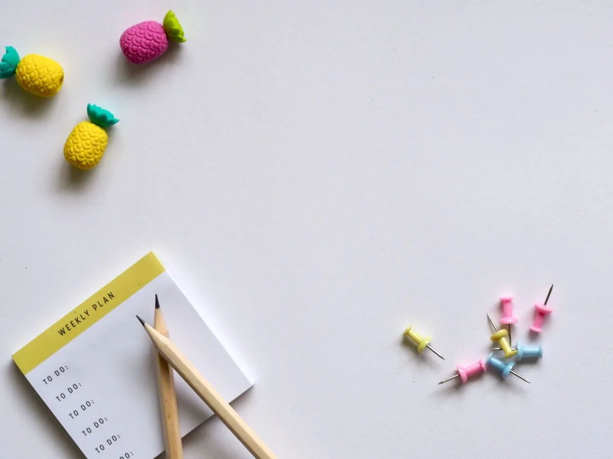 Flat lay of desk items including a planner, pencils, erasers, and push pins on a white background. Flat lay of desk items including a planner, pencils, erasers, and push pins on a white background.
