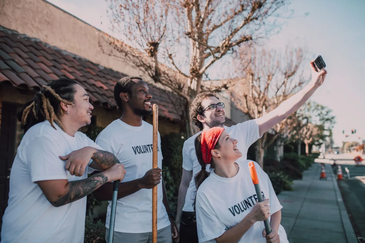 A diverse group of volunteers wearing white shirts and taking a selfie outdoors. A diverse group of volunteers wearing white shirts and taking a selfie outdoors.