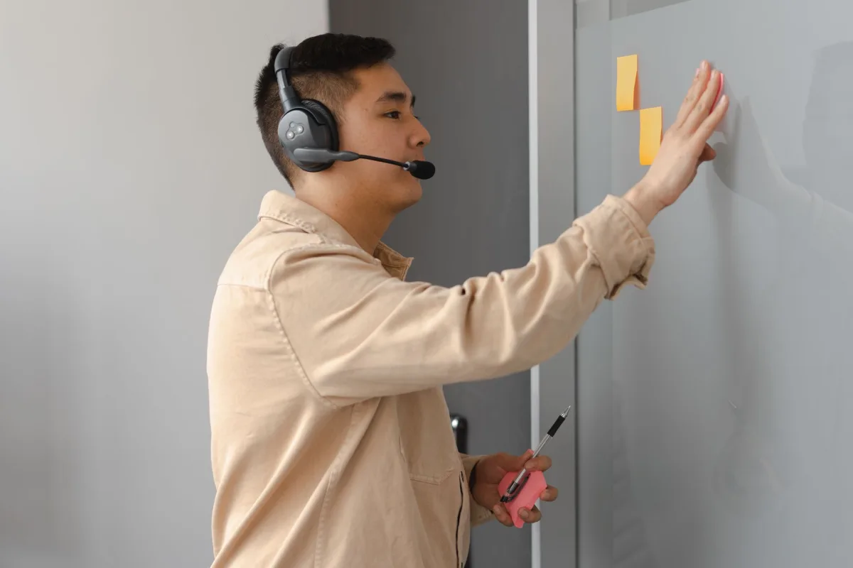 Asian male service agent using sticky notes and headset in an office setting. Asian male service agent using sticky notes and headset in an office setting.