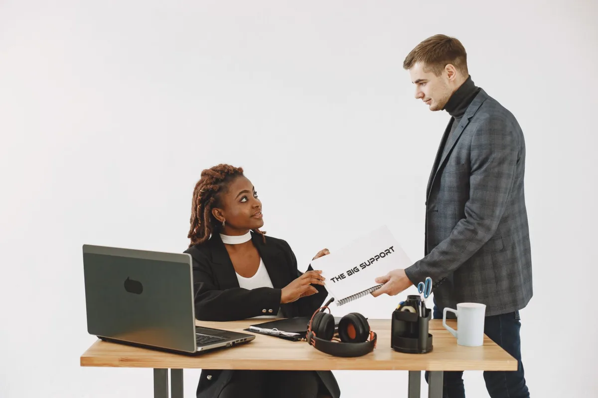 Caucasian man and African American woman collaborating in office with documents and laptop. Caucasian man and African American woman collaborating in office with documents and laptop.