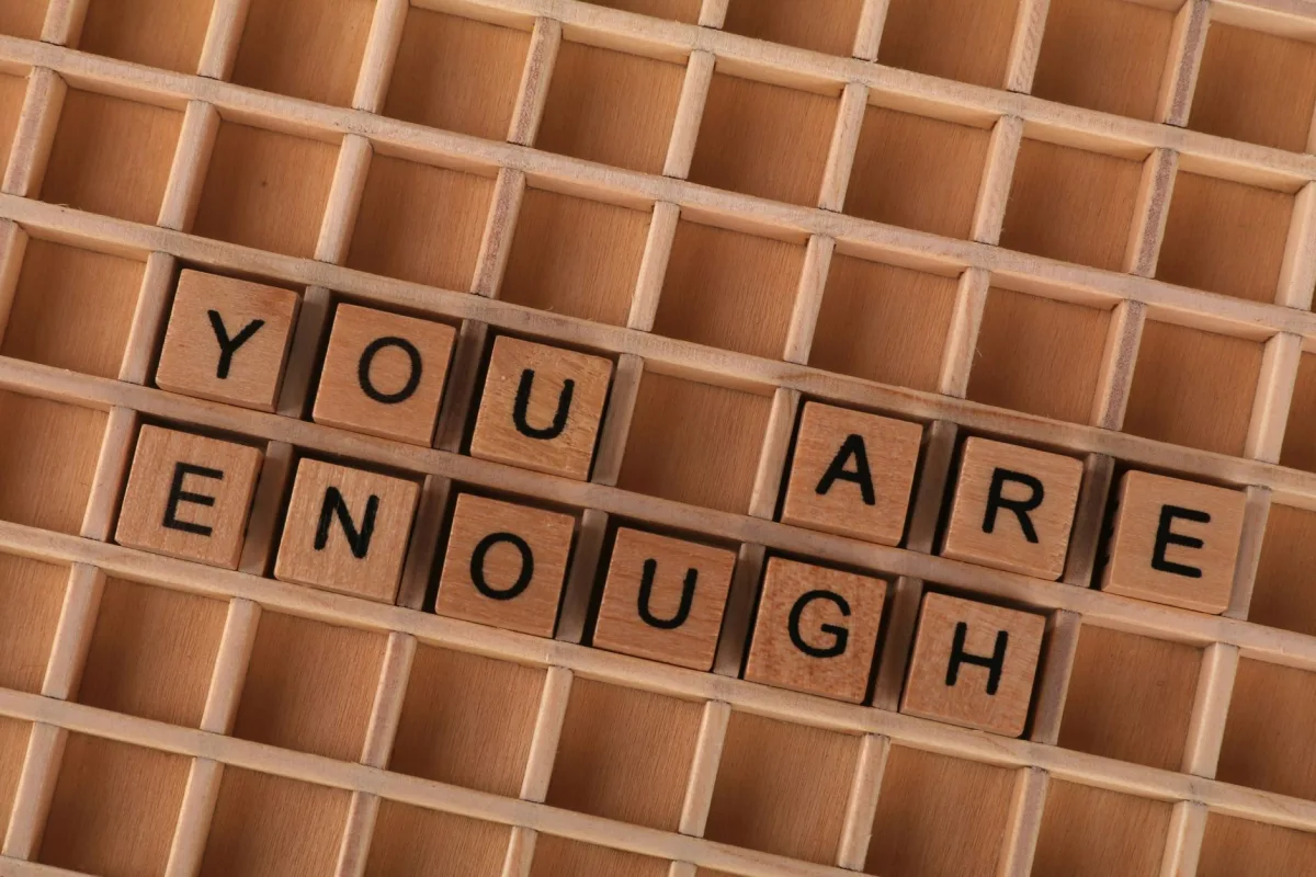 Motivational quote 'You Are Enough' spelled using wooden letter tiles on a wooden grid. Motivational quote 'You Are Enough' spelled using wooden letter tiles on a wooden grid.