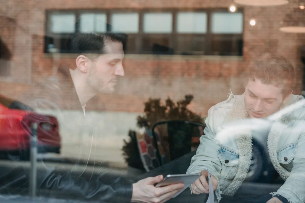 glass of adult modern men in warm jackets sharing tablet while sitting in cafe on daytime glass of adult modern men in warm jackets sharing tablet while sitting in cafe on daytime