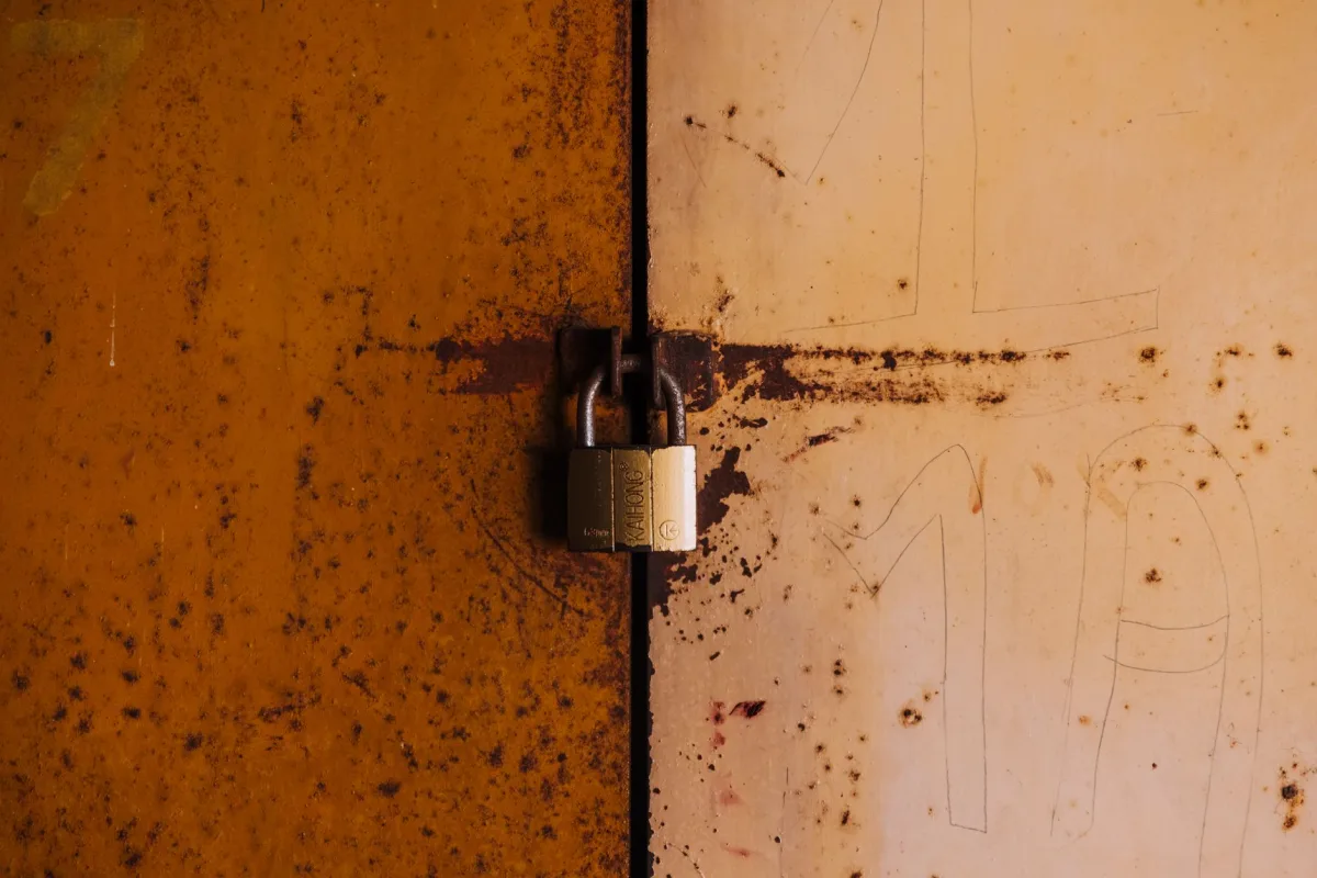 A close-up view of a rusty padlock securing a weathered metal door, highlighting decay and security. A close-up view of a rusty padlock securing a weathered metal door, highlighting decay and security.