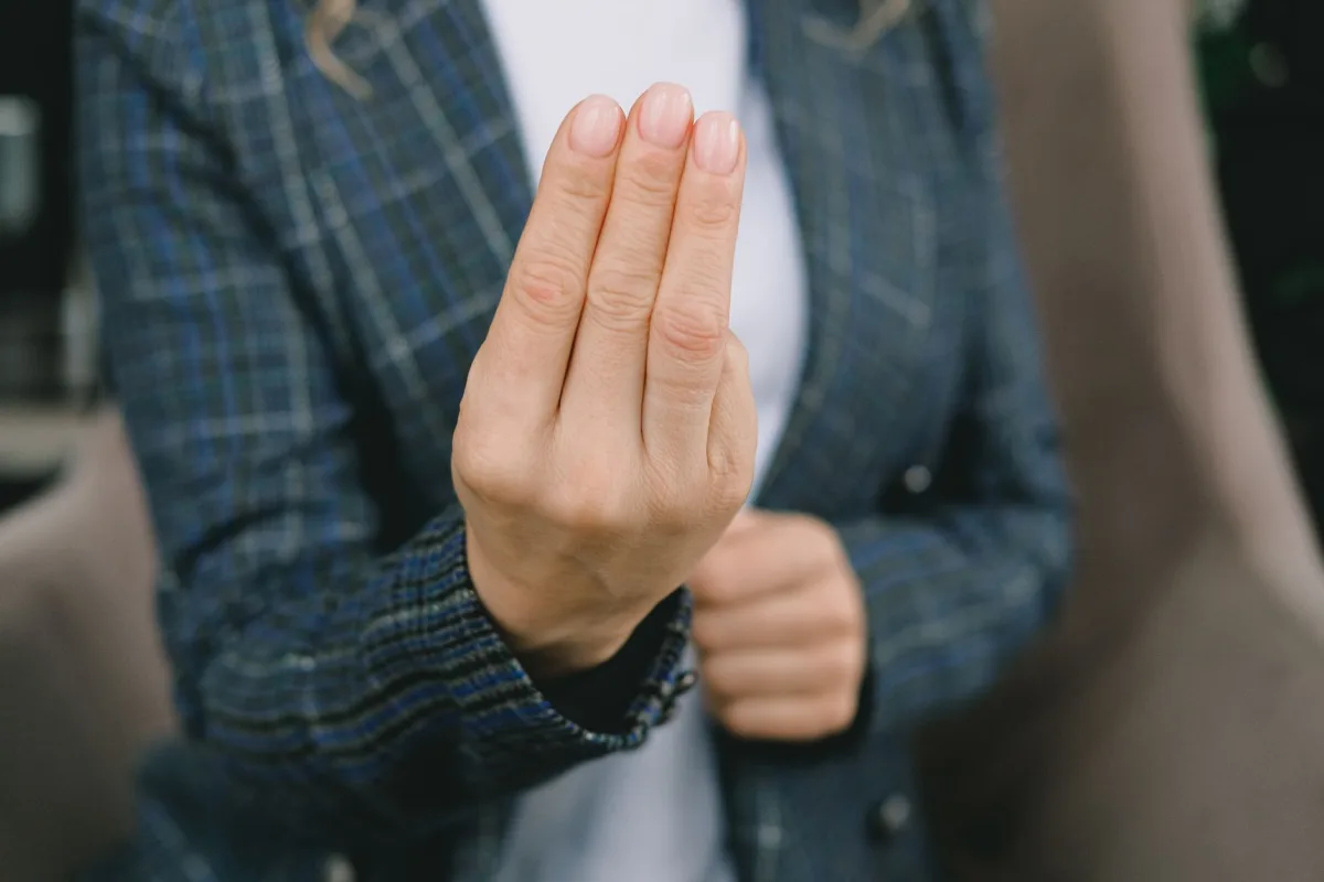 Crop anonymous woman in smart casual outfit sitting in armchair and showing three fingers gesture to camera