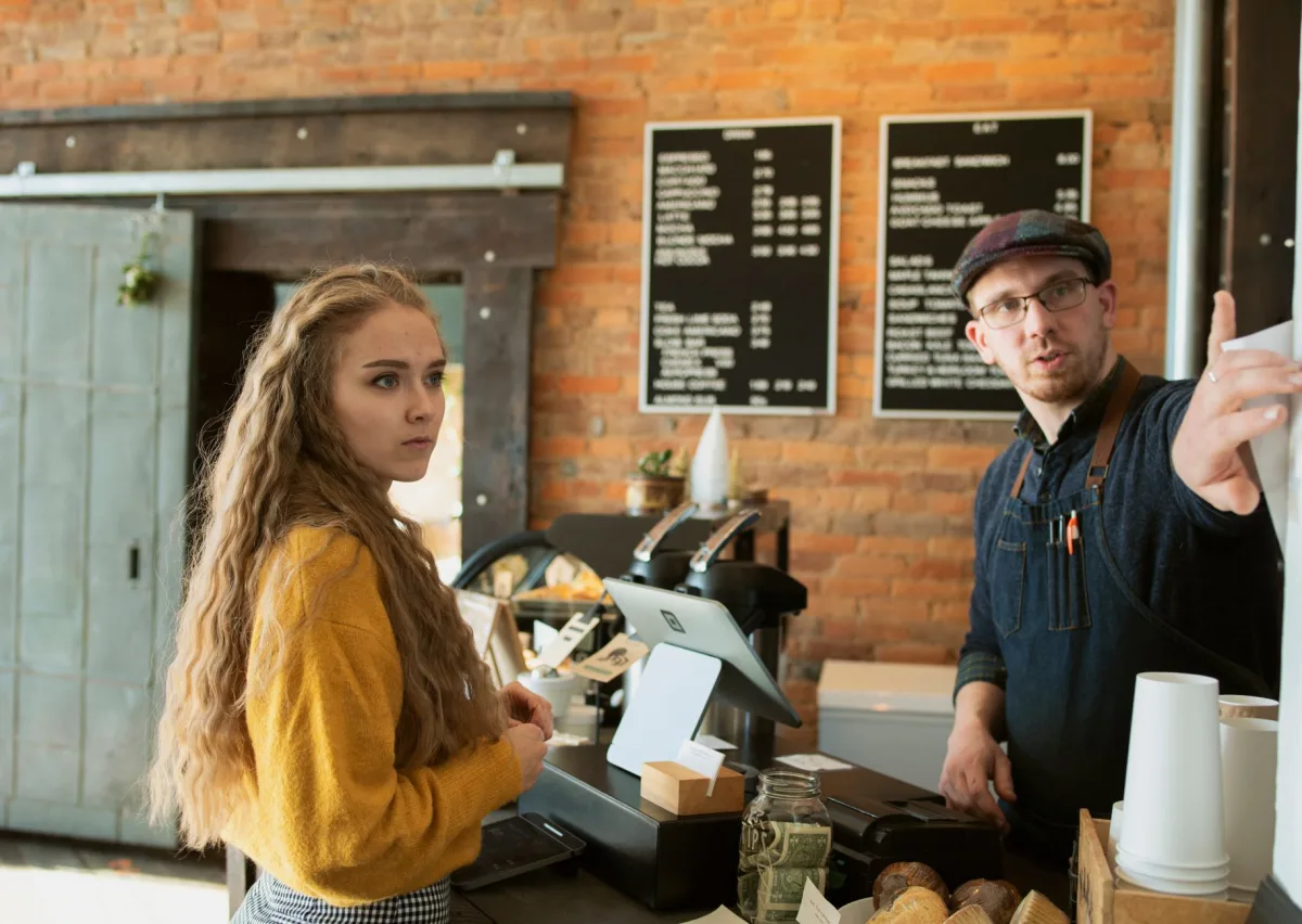 Barista assisting a customer at a coffee shop counter with a visible menu board in the background. Barista assisting a customer at a coffee shop counter with a visible menu board in the background.