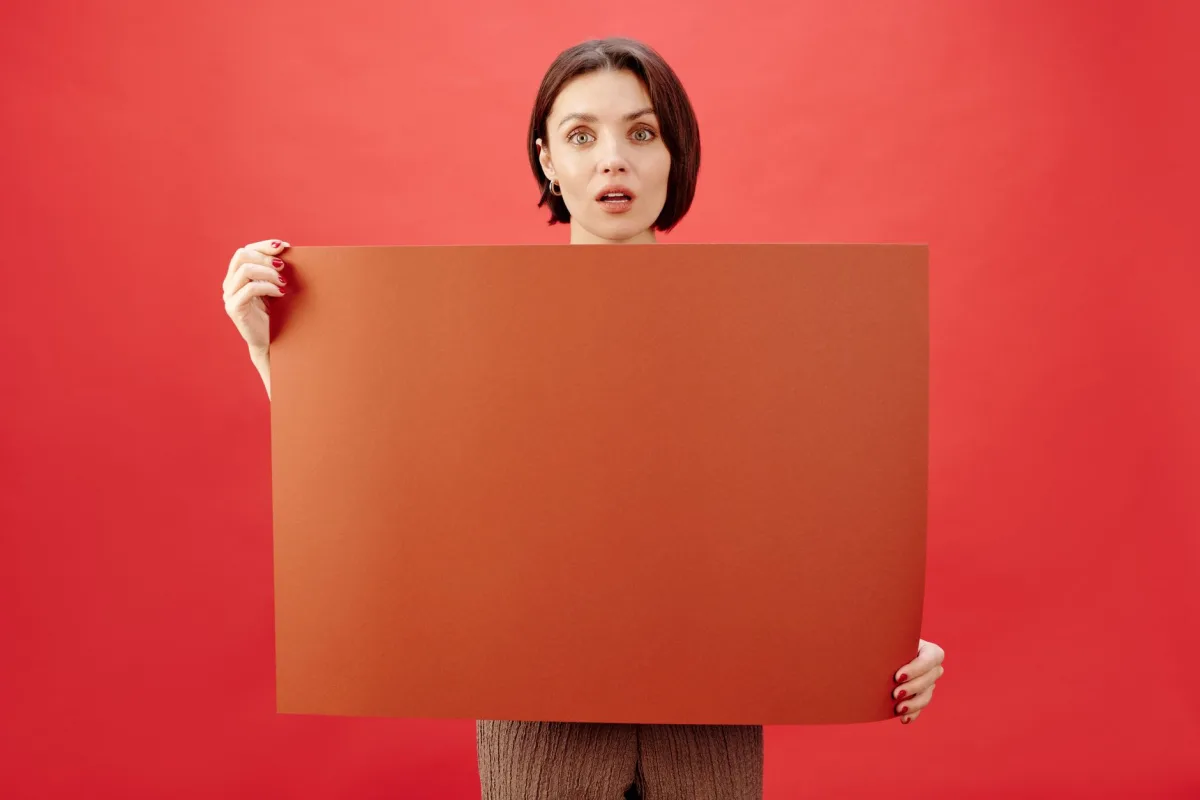A woman holding a brown cardboard on a red background indoors. Perfect for advertising concepts with copy space.