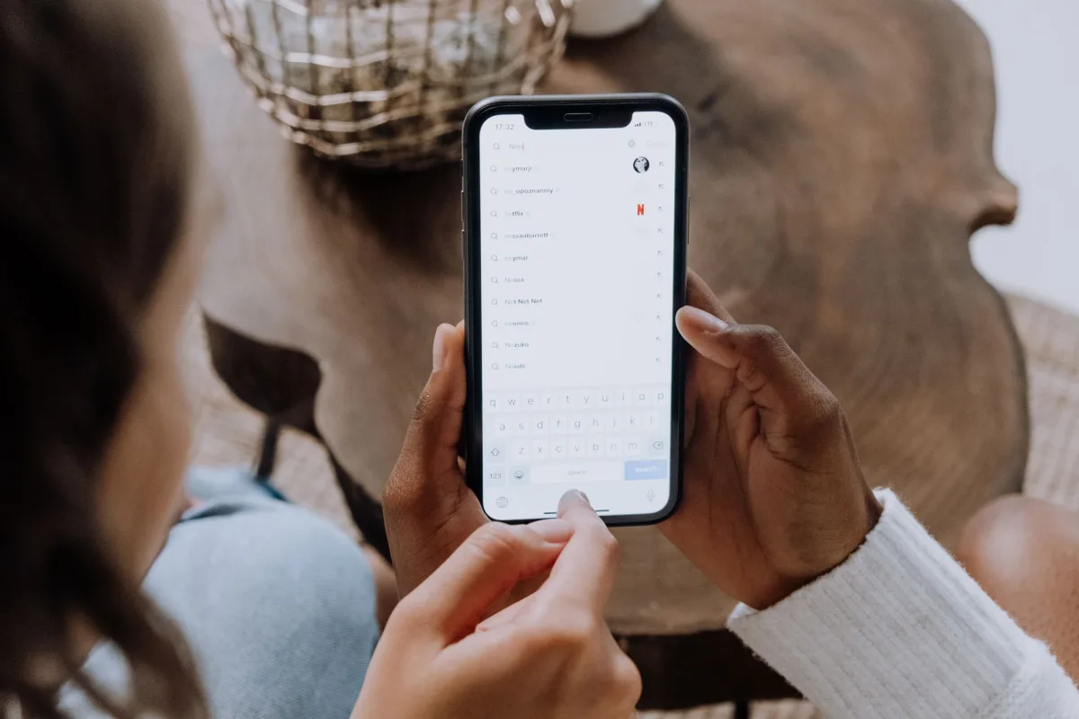 Close-up of hands holding a smartphone, searching for apps like TikTok on a wooden table. Close-up of hands holding a smartphone, searching for apps like TikTok on a wooden table.