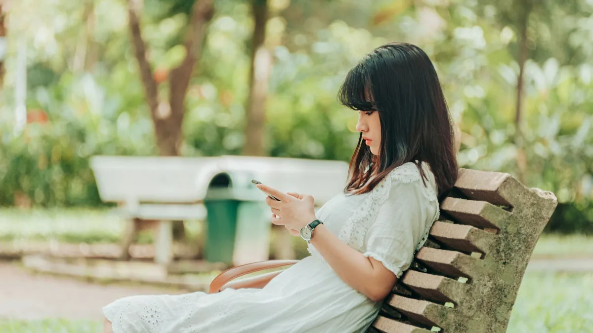 Brunette woman sitting on a park bench enjoying leisure time on her smartphone outdoors. Brunette woman sitting on a park bench enjoying leisure time on her smartphone outdoors.