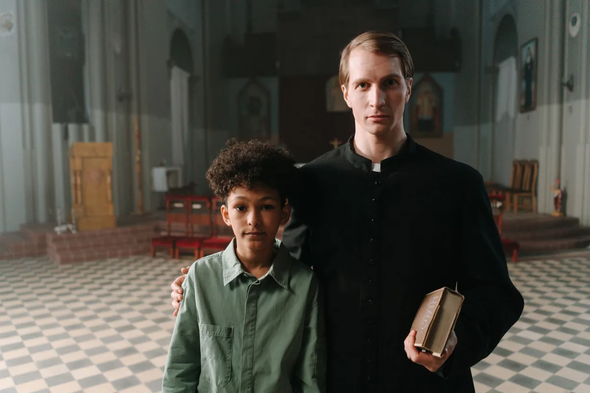 A priest and a boy standing inside a church, symbolizing faith and mentorship. A priest and a boy standing inside a church, symbolizing faith and mentorship.