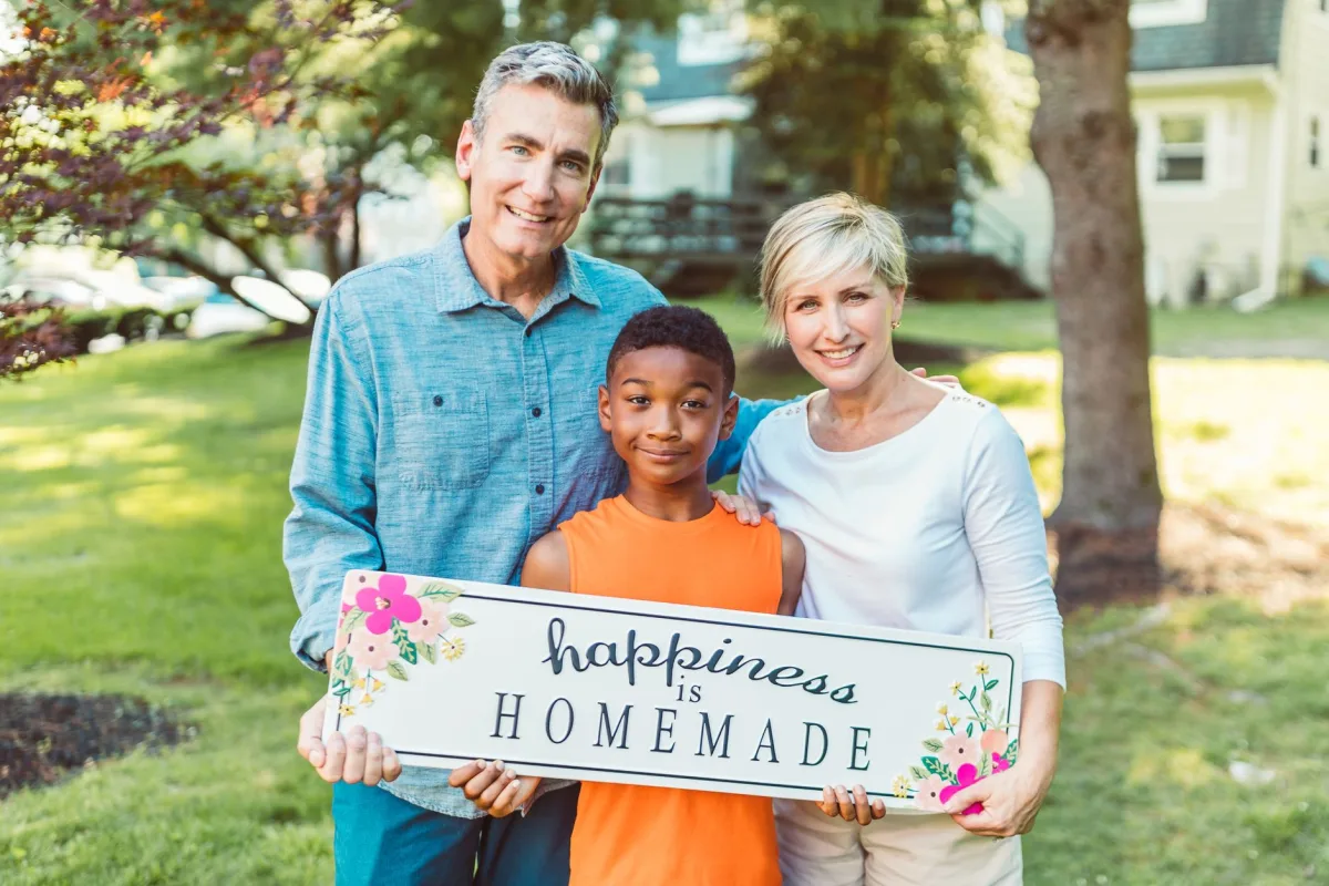 A joyful family embraces togetherness holding a happiness sign outdoors.