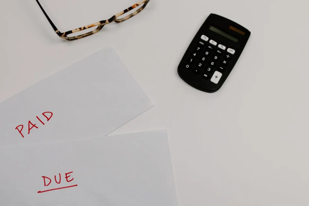 Top view of financial papers labeled 'Paid' 'Due' beside a calculator glasses.