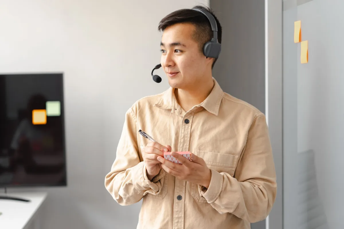 Smiling Asian man with headset holding notes, representing service in an office. Smiling Asian man with headset holding notes, representing service in an office.