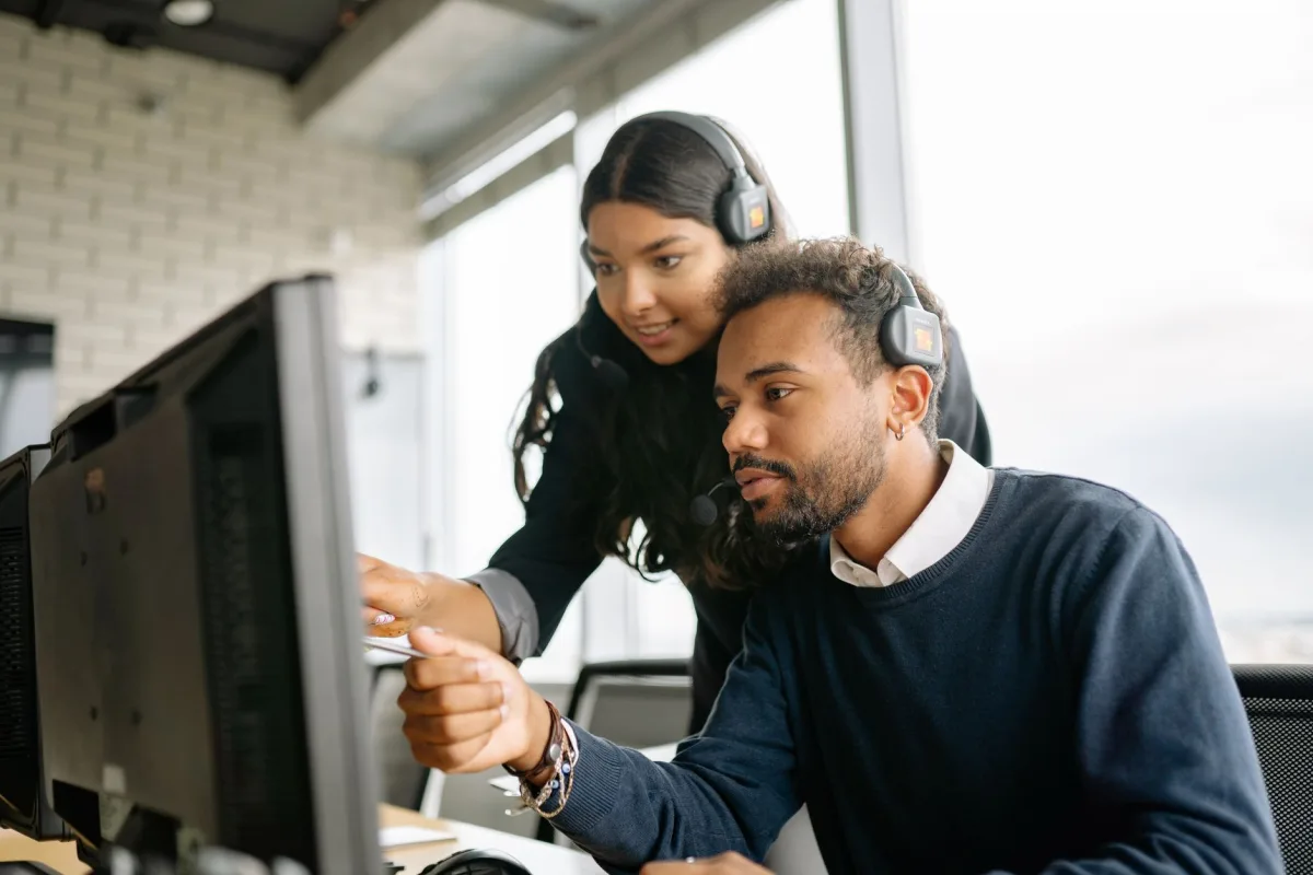Two call center employees working together with headsets in a modern office setting. Two call center employees working together with headsets in a modern office setting.