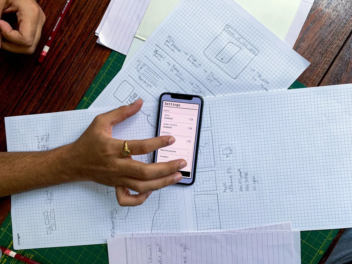 Hand holding smartphone over app design sketches on papers, top view. Hand holding smartphone over app design sketches on papers, top view.