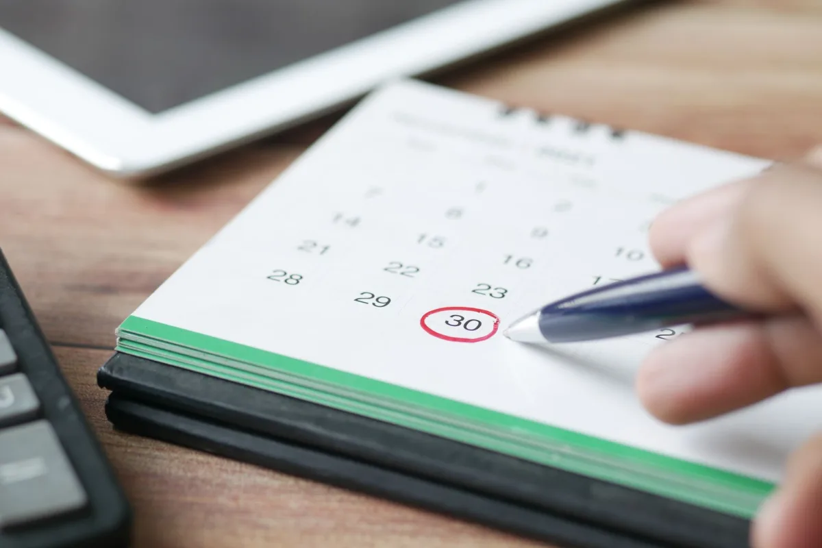 Close-up shot of a hand marking a date on a calendar with a pen, emphasizing planning and scheduling. Close-up shot of a hand marking a date on a calendar with a pen, emphasizing planning and scheduling.