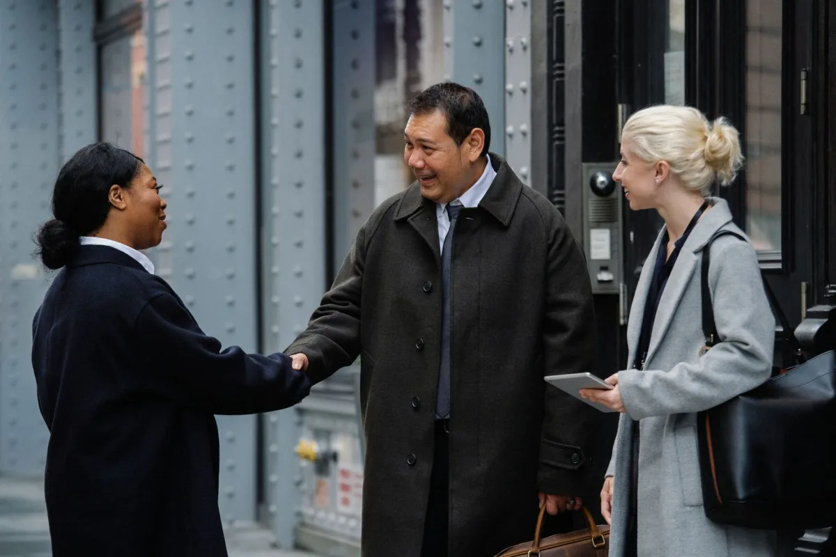 Cheerful multiracial business partners in elegant outfits shaking hands of each other while standing on street before meeting Cheerful multiracial business partners in elegant outfits shaking hands of each other while standing on street before meeting