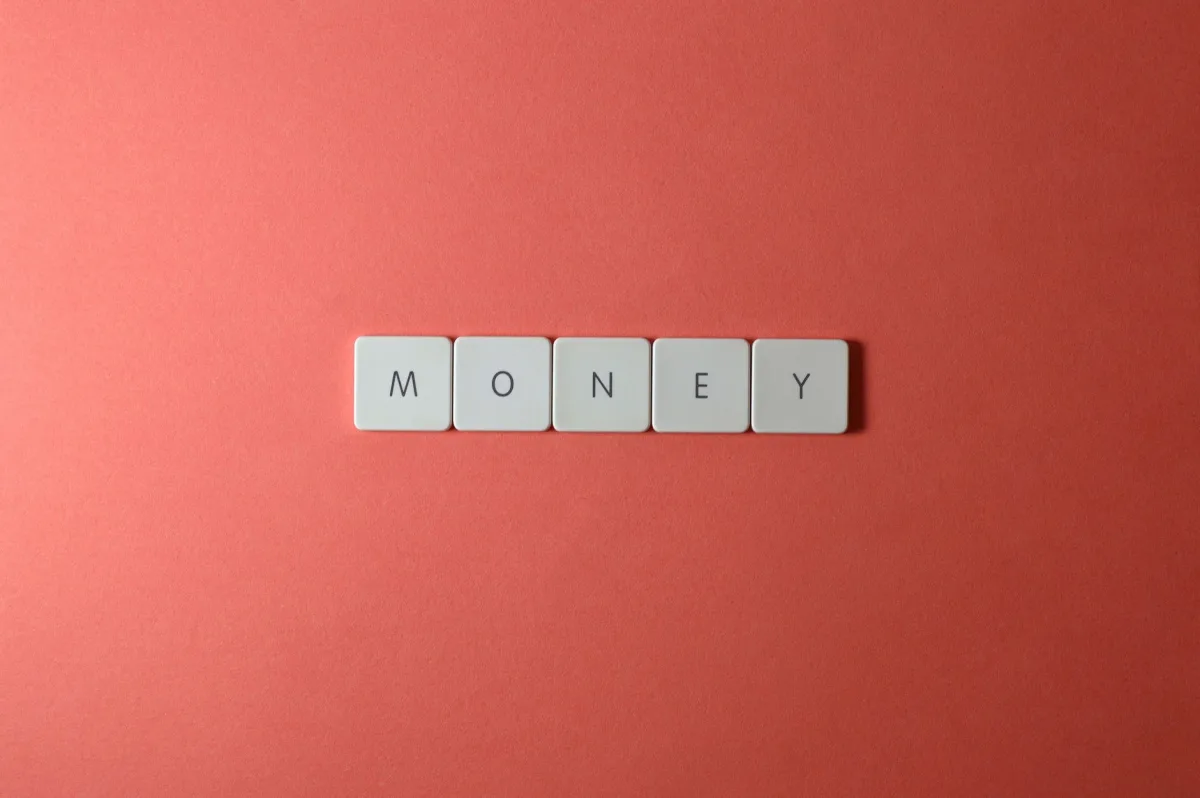 Minimalist layout showing word 'money' with letter tiles on a coral background. Minimalist layout showing word 'money' with letter tiles on a coral background.