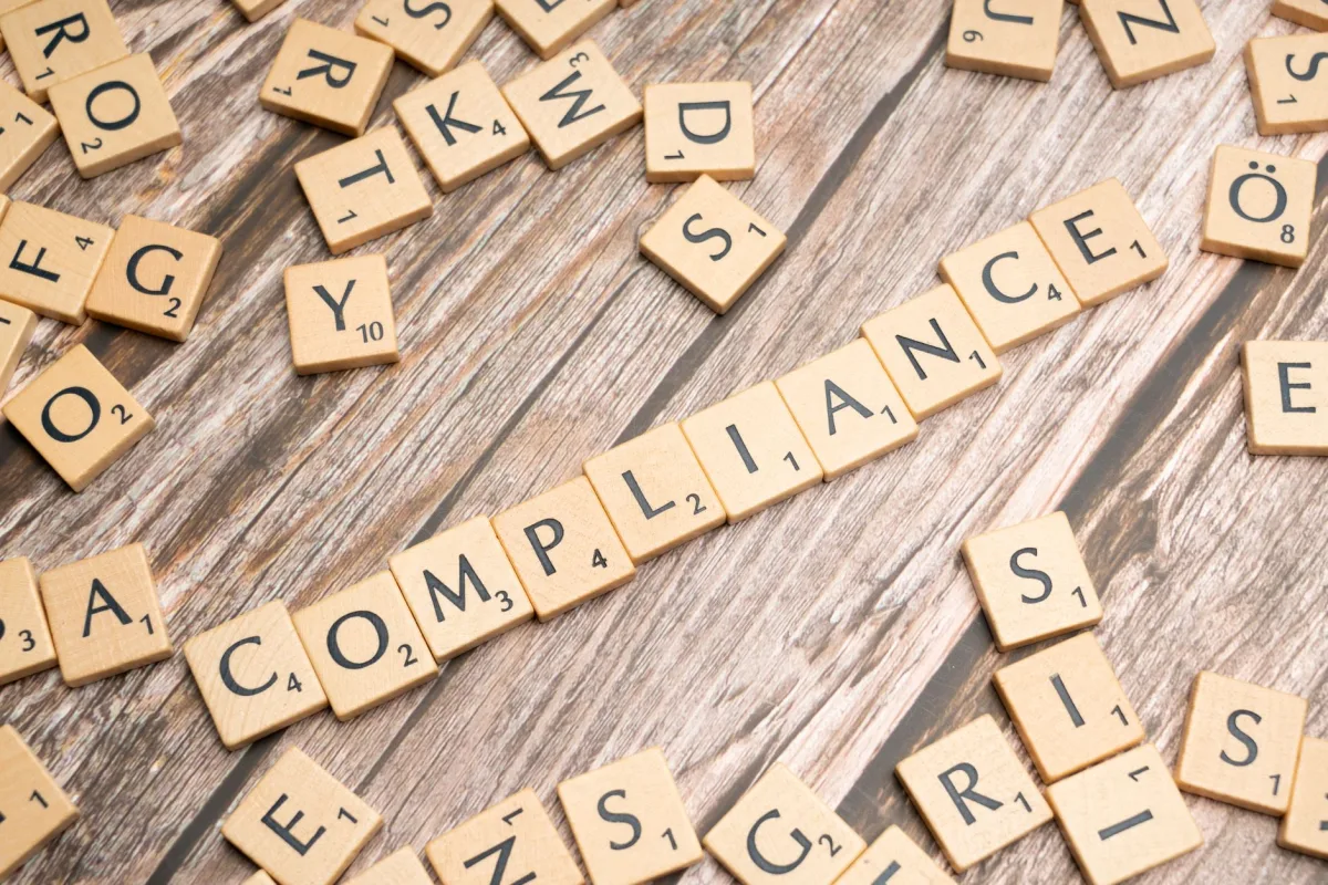 Wooden letter tiles forming the word 'COMPLIANCE' on a rustic wooden background. Wooden letter tiles forming the word 'COMPLIANCE' on a rustic wooden background.