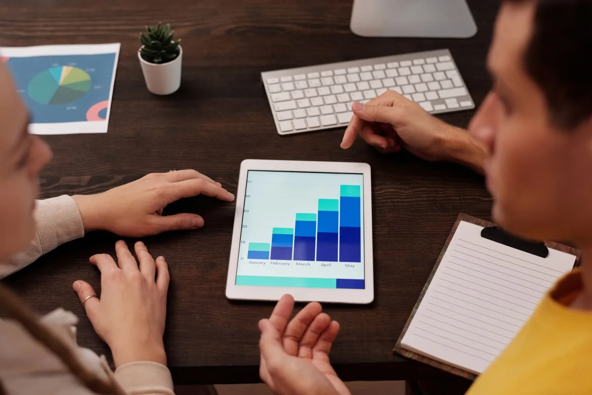 Team members discussing graphs on a tablet in a modern office setting. Team members discussing graphs on a tablet in a modern office setting.