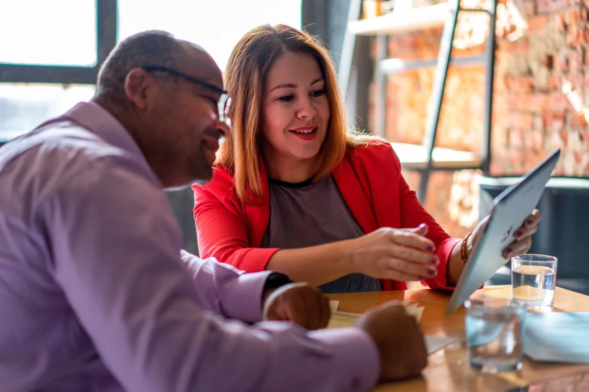 Two adults engaged in a productive conversation using a tablet in a modern office setting. Two adults engaged in a productive conversation using a tablet in a modern office setting.