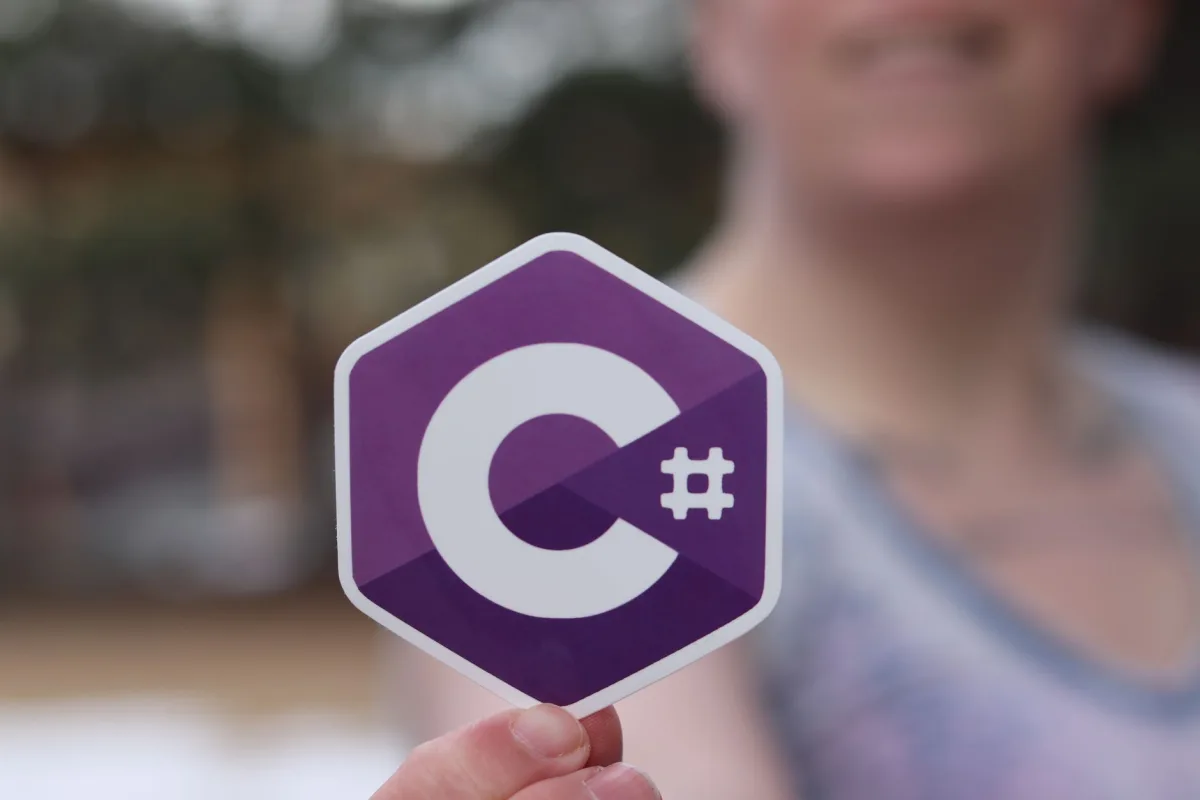 Person holding a C# programming language logo sticker outdoors. Person holding a C# programming language logo sticker outdoors.