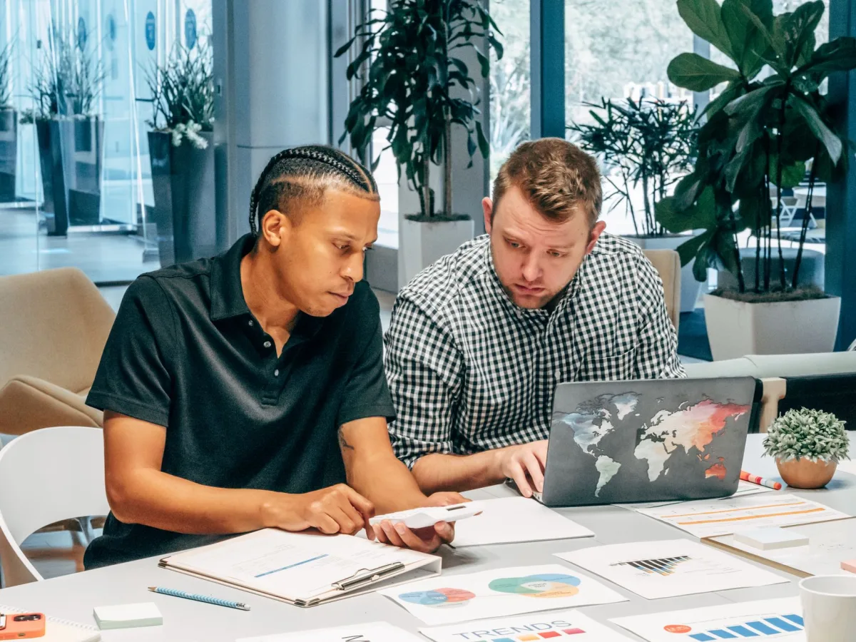 Two men working together in a modern office with laptops and documents, discussing Two men working together in a modern office with laptops and documents, discussing