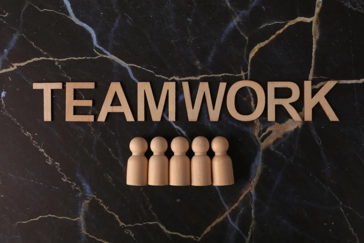 Wooden figures arranged under 'TEAMWORK' on a marble background symbolizing collaboration.