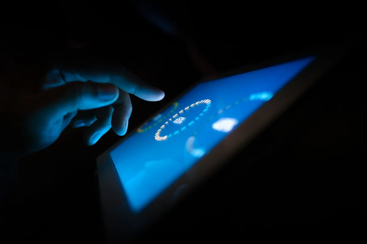 Close-up of a hand interacting with a glowing touchscreen in a dark setting, highlighting technology use. Close-up of a hand interacting with a glowing touchscreen in a dark setting, highlighting technology use.