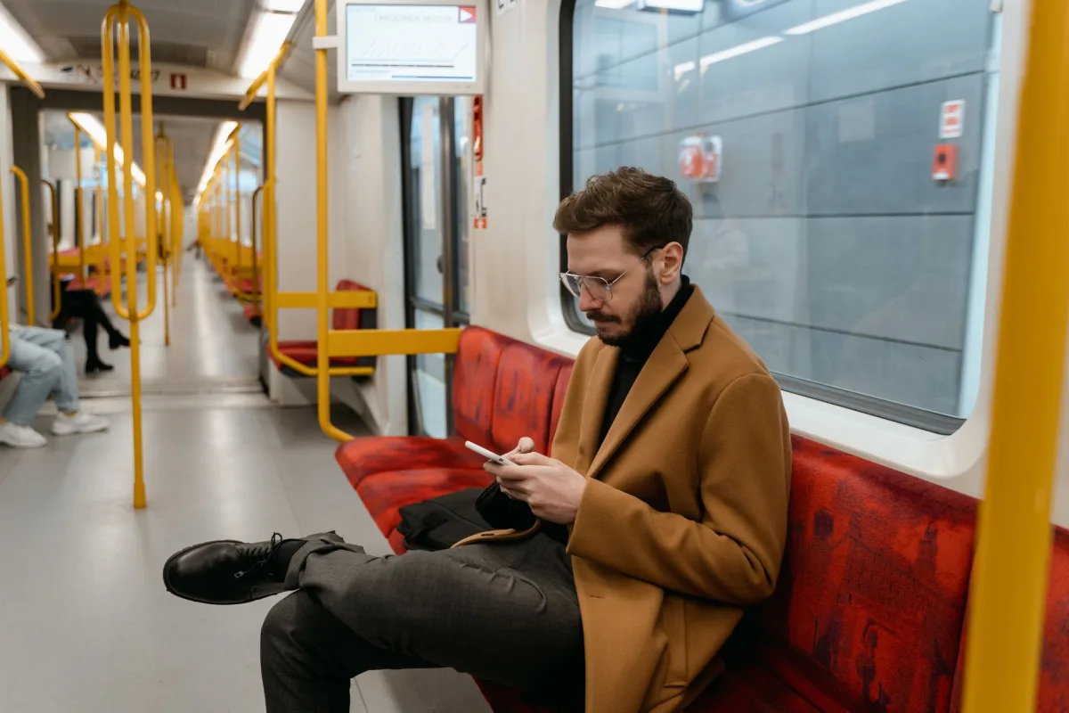 Bearded man in brown coat texting on a train with red seats. Commuting lifestyle scene. Bearded man in brown coat texting on a train with red seats. Commuting lifestyle scene.