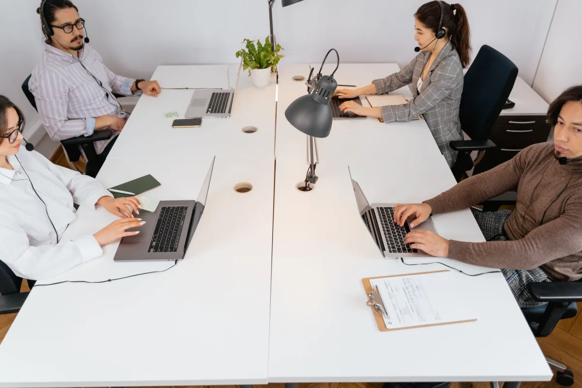 Team of four in a modern office setting using laptops and headsets for communication. Team of four in a modern office setting using laptops and headsets for communication.
